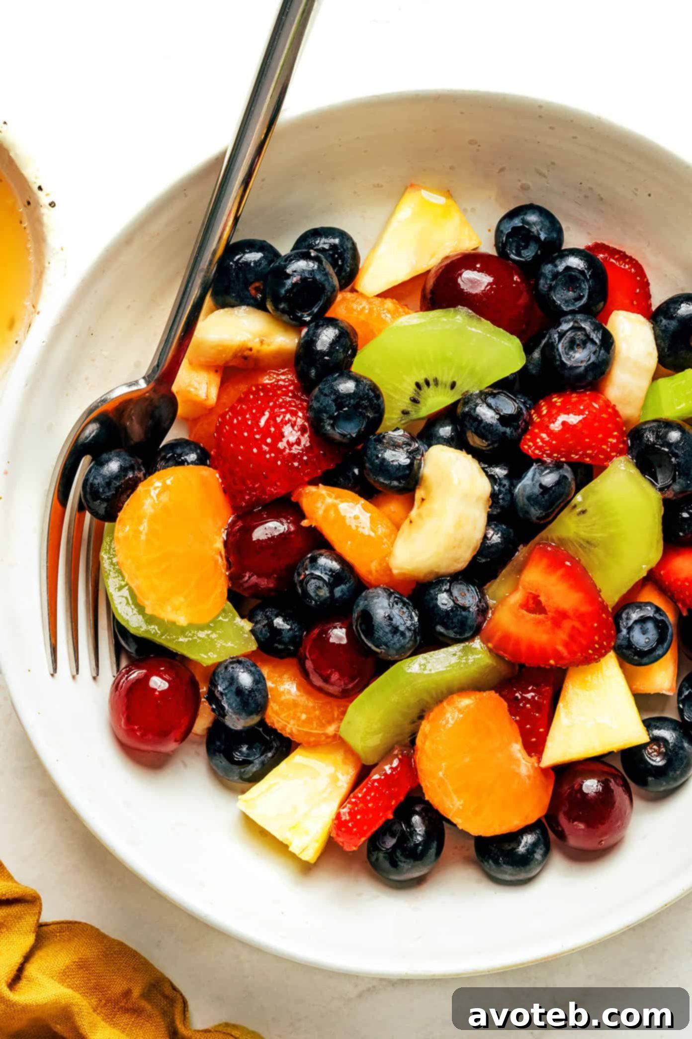 A single serving of fruit salad in a small bowl, with a fork digging in, showing the vibrant colors and freshness of the fruits.