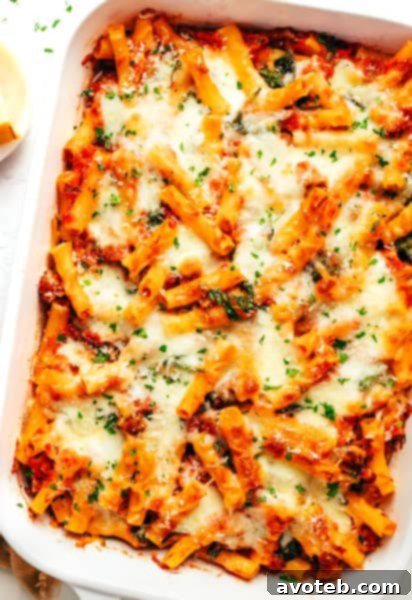 Baked Ziti with a serving spoon, garnished with herbs