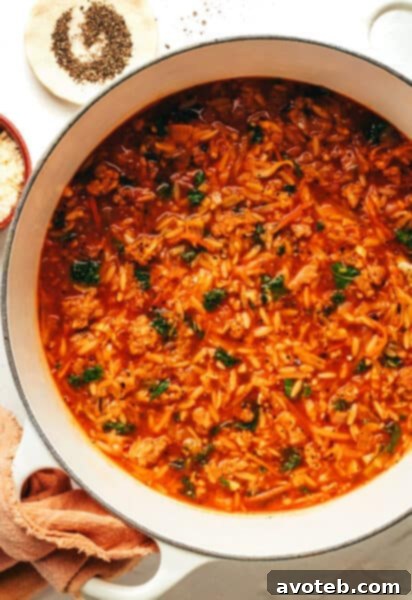 A bowl of Cabbage Sausage Orzo Soup on a wooden surface.
