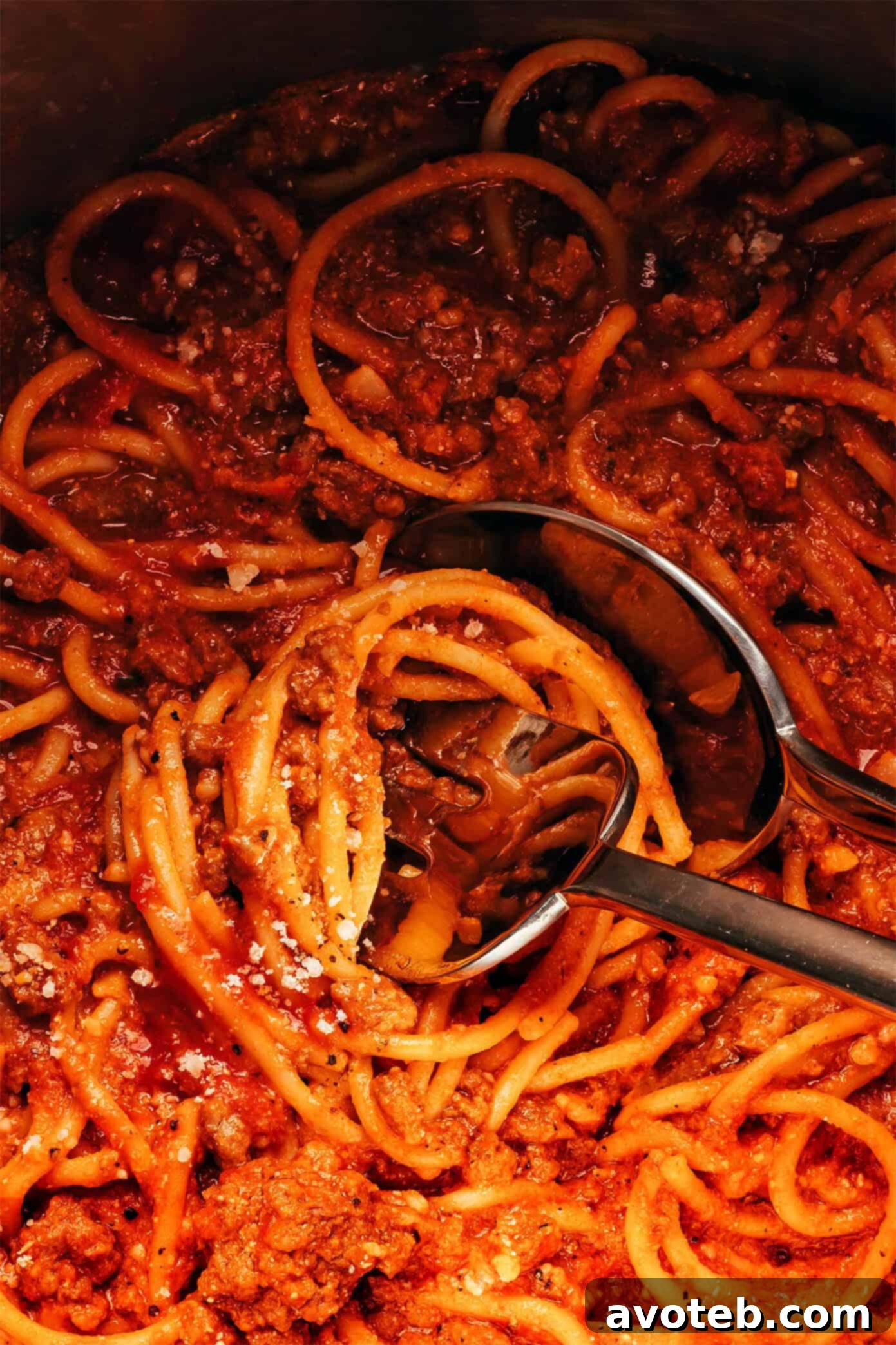 A top-down view of High Protein Instant Pot Spaghetti in a pot with serving spoons.