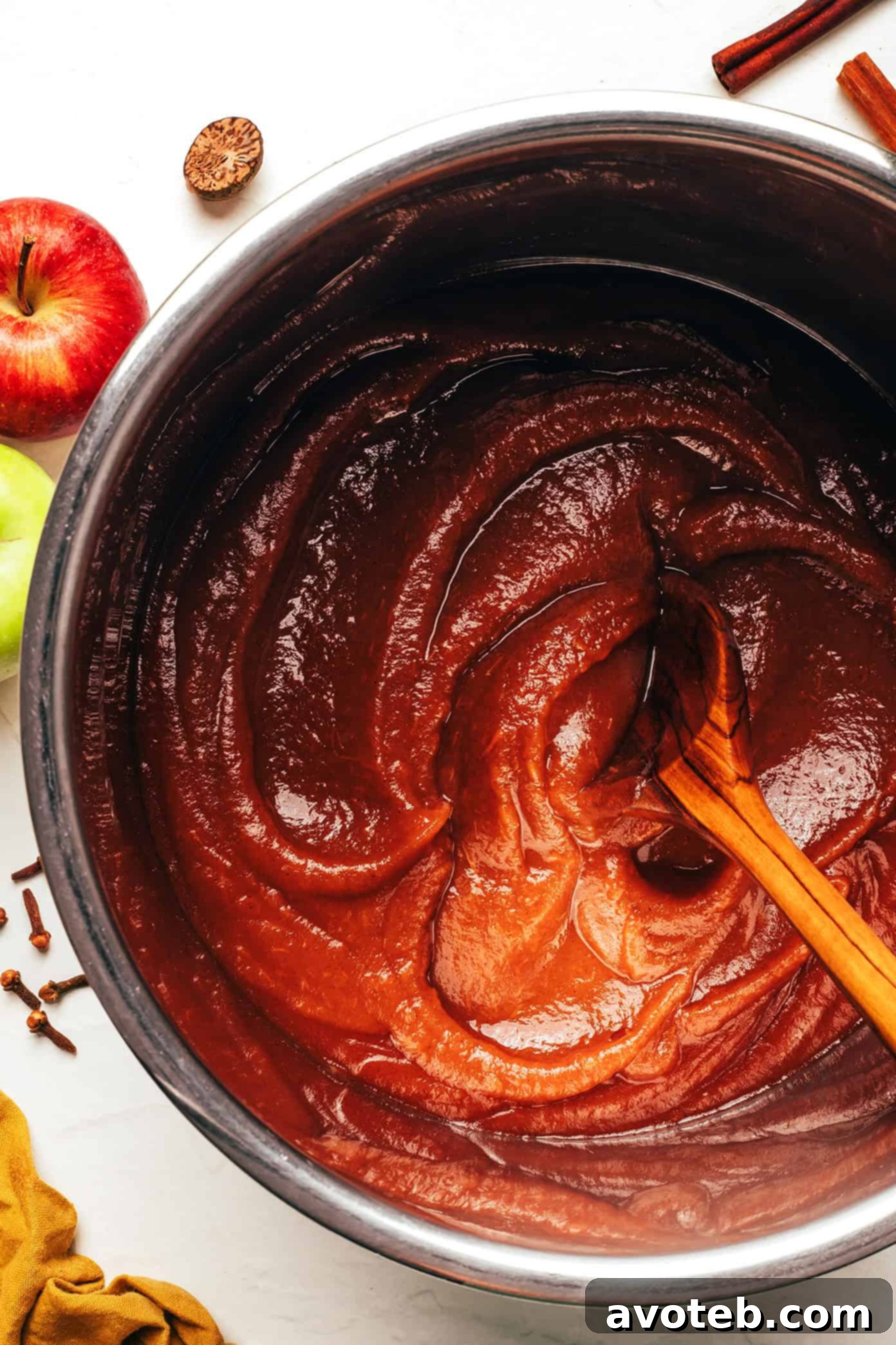 A jar of homemade apple butter, rich brown in color, with a spoon resting on the side.