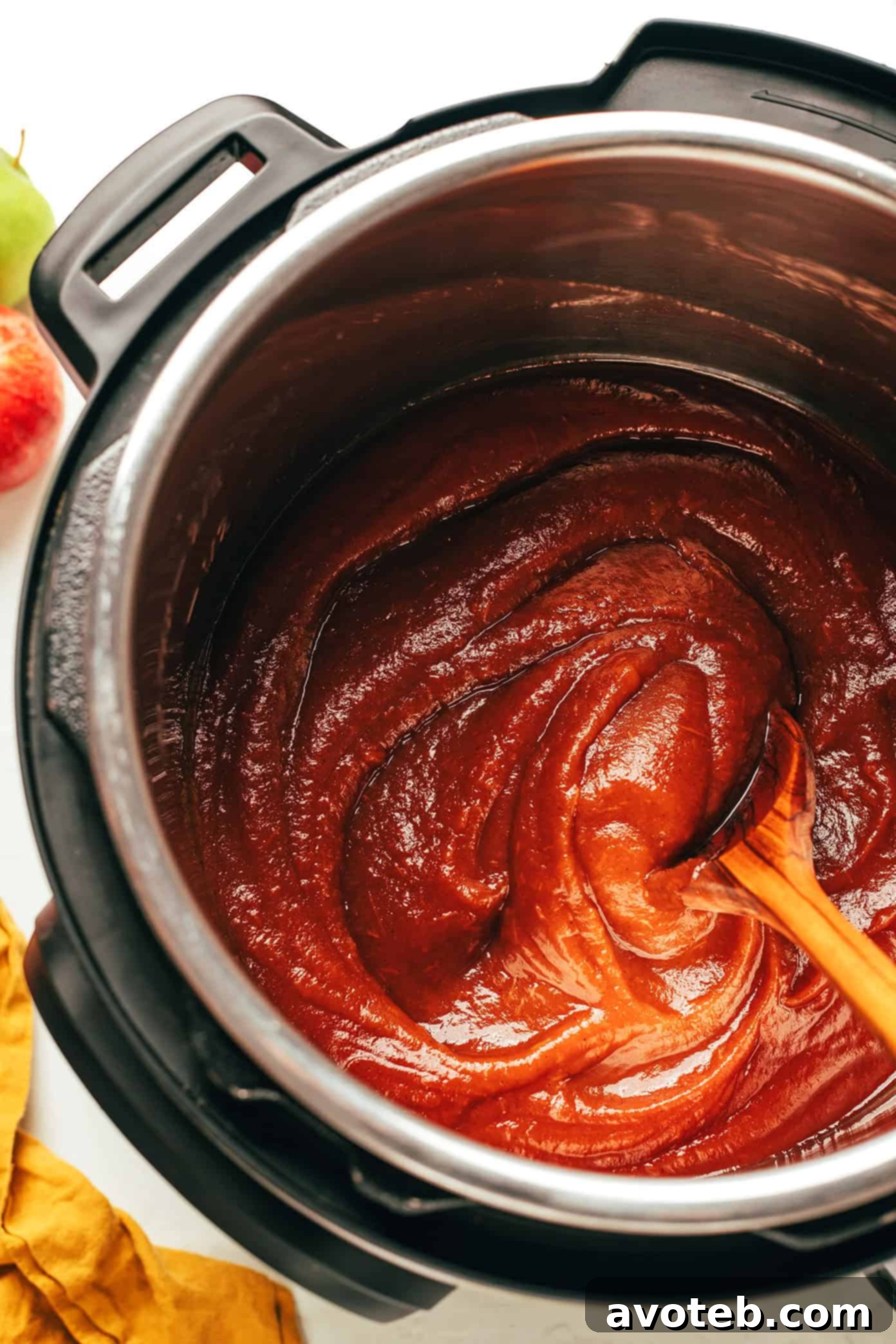 A close-up of a jar of apple butter being scooped with a spoon, highlighting its creamy texture.