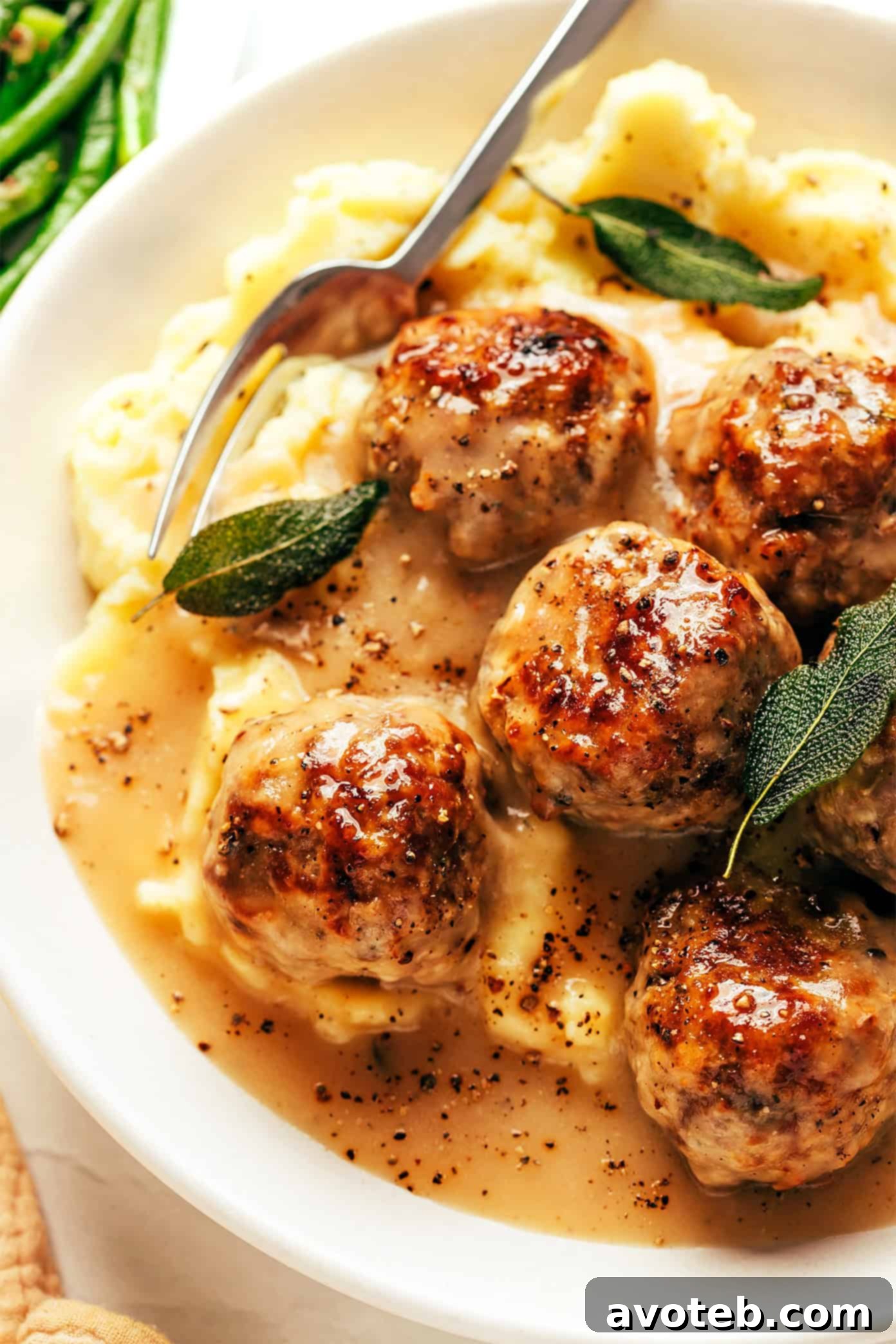 Hearty Turkey Meatballs Smothered in Gravy 6 A serving of turkey meatballs with gravy, garnished with fresh sage, ready to be enjoyed with mashed potatoes.