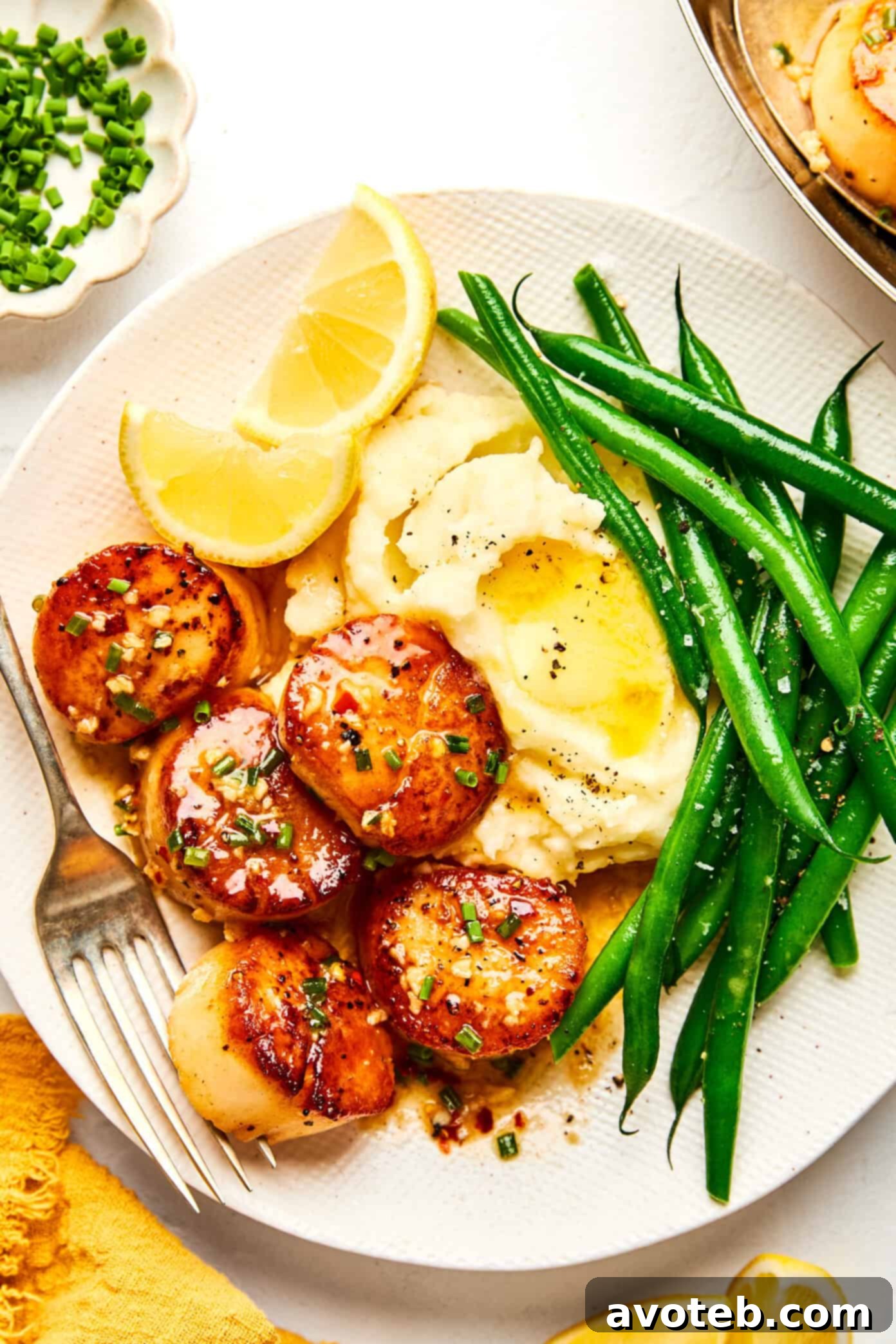 Lemon-Kissed Scallops with Garlic Butter Glaze 8 Seared scallops dinner on a plate with mashed potatoes, green beans, and lemons.