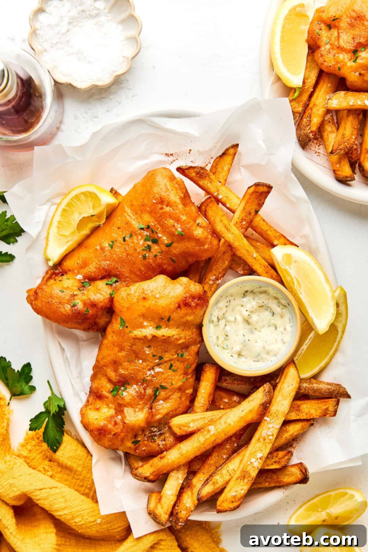 A vibrant spread of freshly prepared Old Bay Fish and Chips, garnished with parsley and lemon wedges.